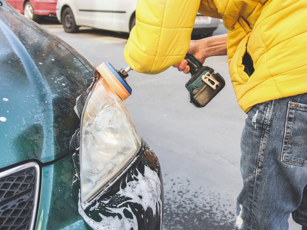 A young Caucasian guy drilling with a sponge disk polishes the headlight.