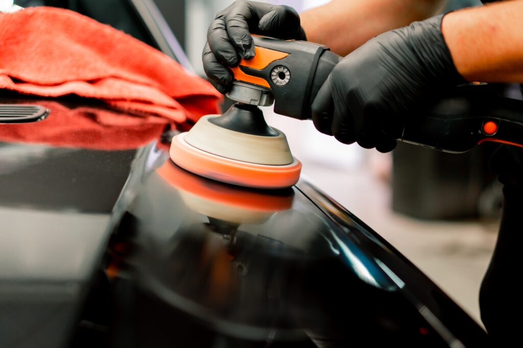 Close-up of a car wash worker using a polishing machine to polish the hood of black luxury car