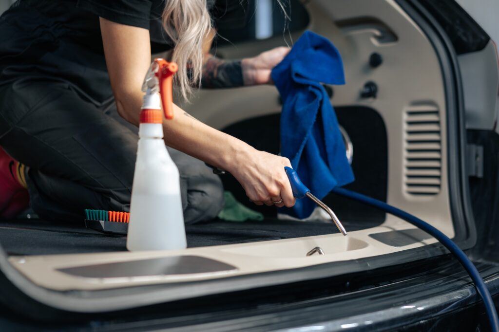 Woman cleaning car salon with polishing spray in car detailing service