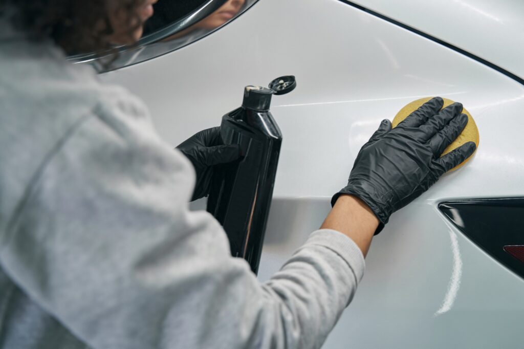 Worker in nitrile gloves waxing client motorcar